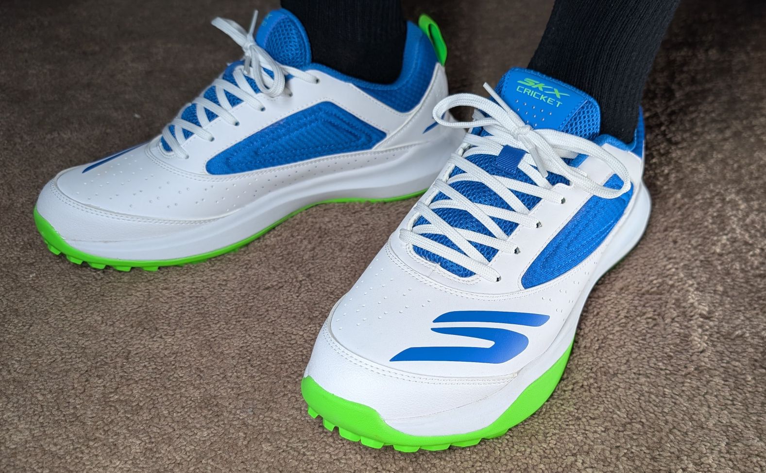 Blue, green, and white Skechers Turf Cricket shoes on feet