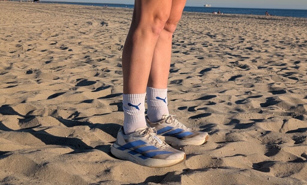 Runner standing in white puma socks and white and blue Adidas Adizero EVO SL super trainers next to the ocean