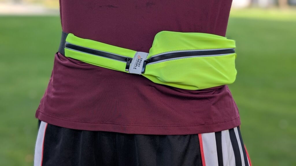 Close up of iPhone in pocket of Sport2People fluorescent running belt on the waist of Our Three Cents reviewer in red shirt