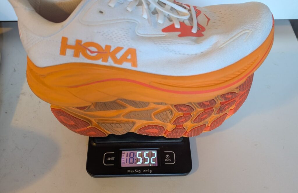 Hoka Clifton 10 white and orange running shoes weighed on scale showing 552 grams