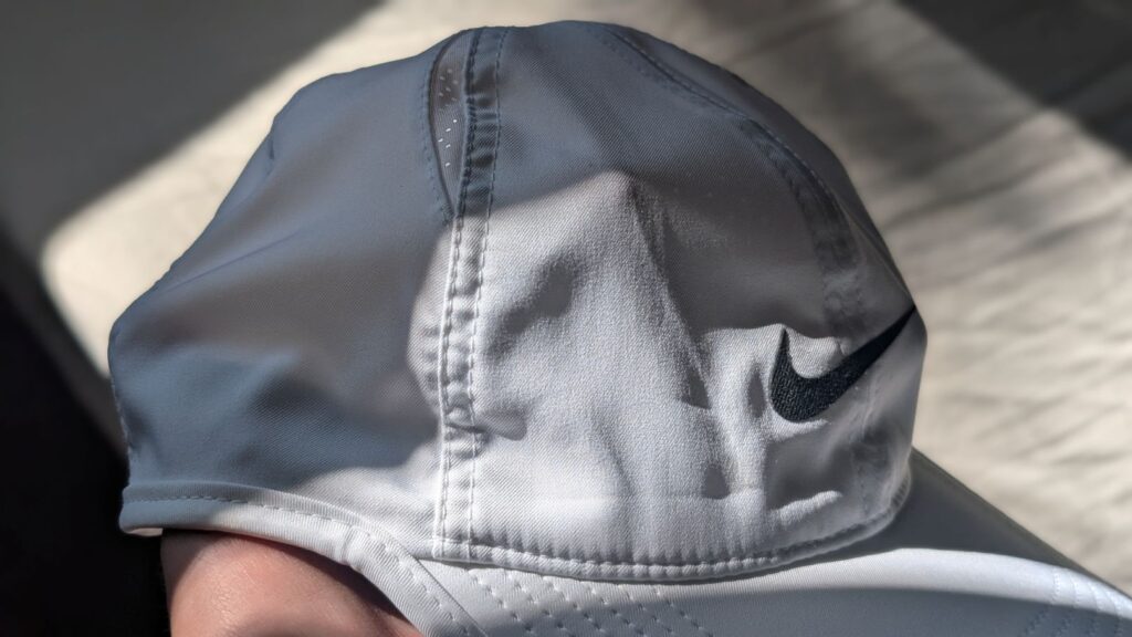Hand showing the see-through lightweight fabric of a white Nike of the Dri-FIT Club Unstructured Featherlight Cap