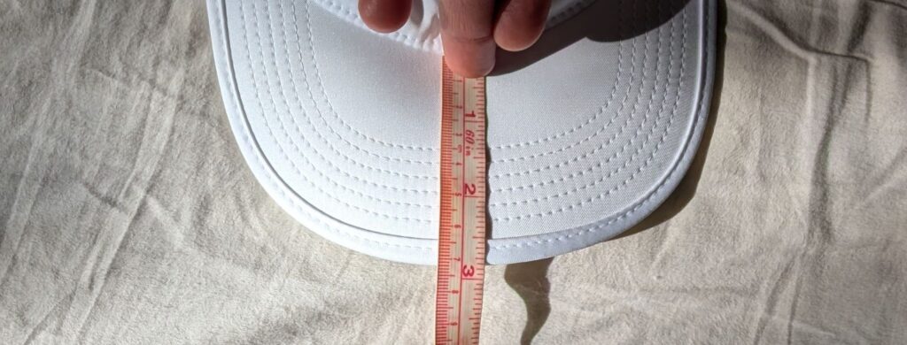 Measuring tape on white Nike FB5682 Running Cap showing visor length over 7 cm.