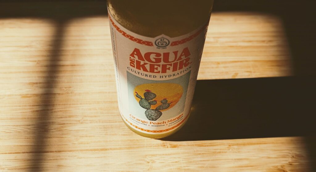 Bottle of GTs Agua de Kefir Orange Peach Mango Cultured Hydration Drink in sunshine showing health benefits