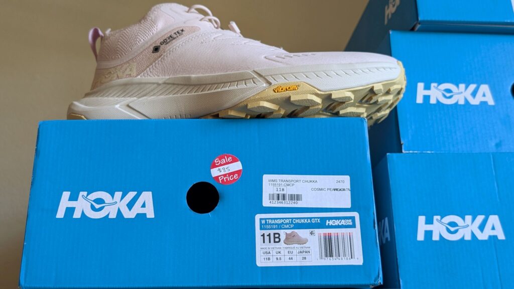 Close up on pink Hoka Transport Chukka GTX shoe on blue box with $85 sale sticker