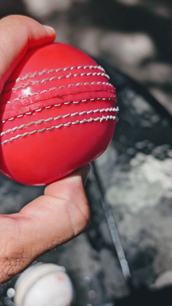 Thumb pressing pink synthetic cricket ball to show hardness